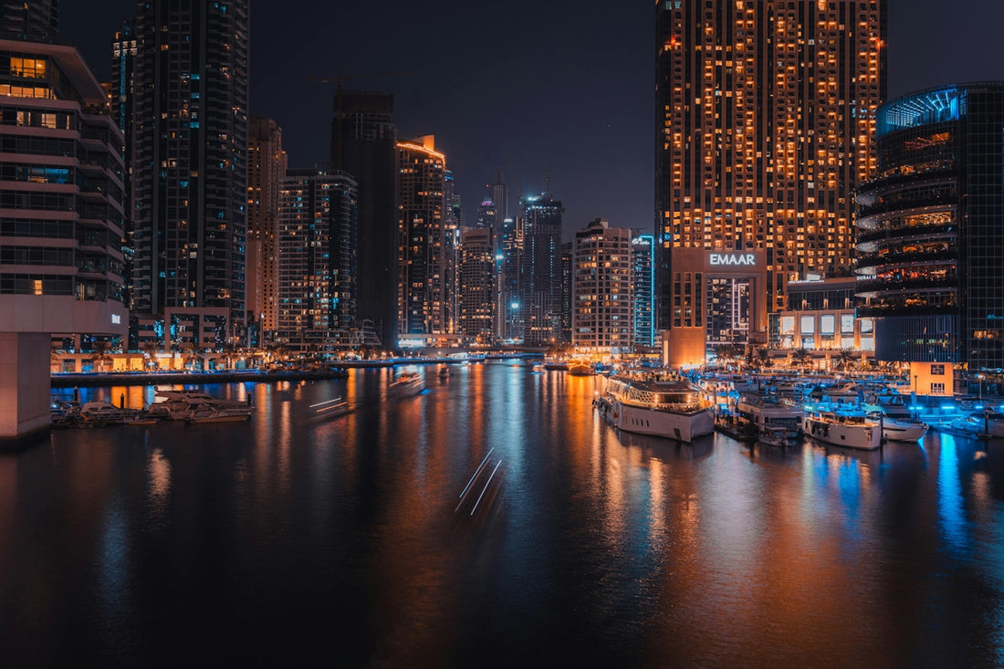 Modern cityscape with illuminated skyscrapers and boats at night.