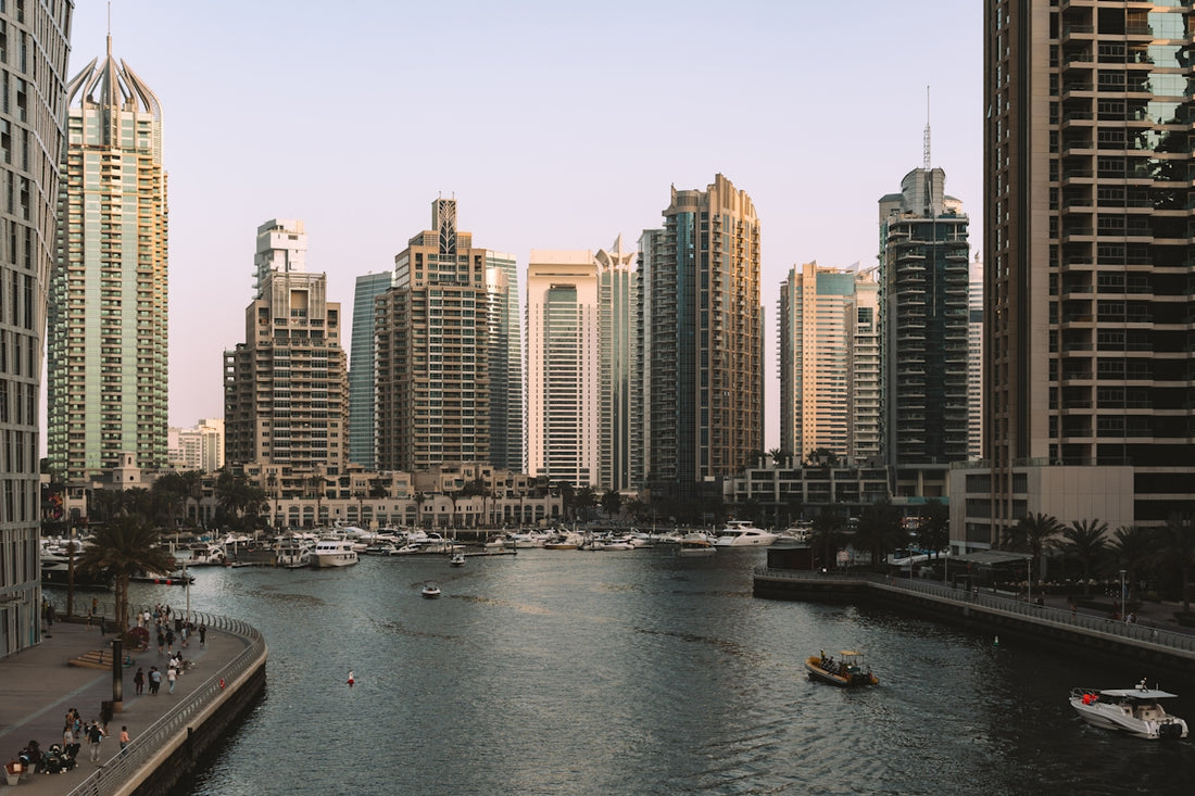 Modern skyscrapers line a tranquil canal with docked boats.