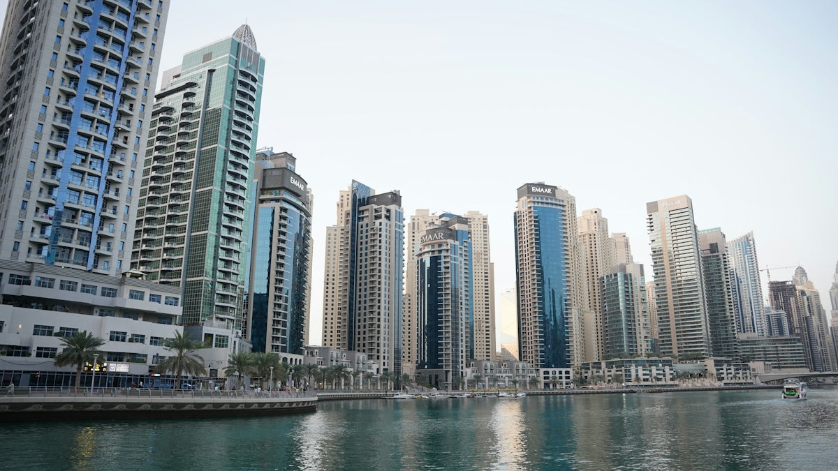 Modern skyscrapers along the Dubai Marina waterfront with palm trees and a boat